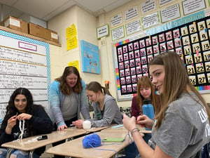 Students learning knitting from a teacher.