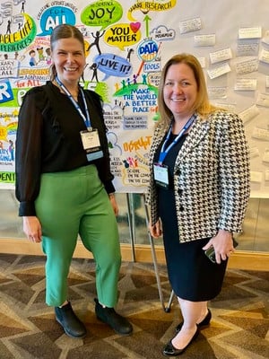 Maggy Olson and Kim Amidzich standing in front of a poster with affirmations