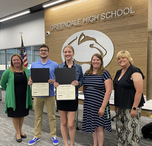 Five people standing together and smiling with two students holding certificates.